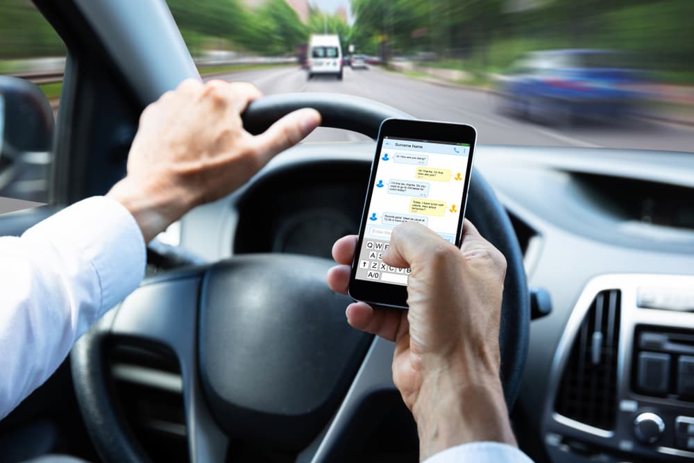 Man using cell phone to text while driving down the road