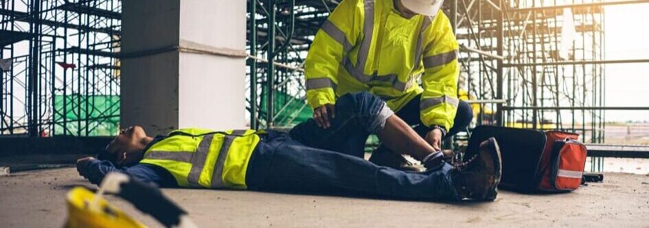 construction worker helping injured coworker lying on ground after accident