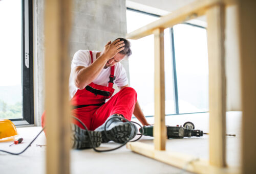 Worker sitting on flor holding his head after a head injury in construction site