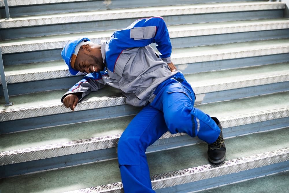 worker dressed in blue and gray uniform laying on steps holding lower back in pain