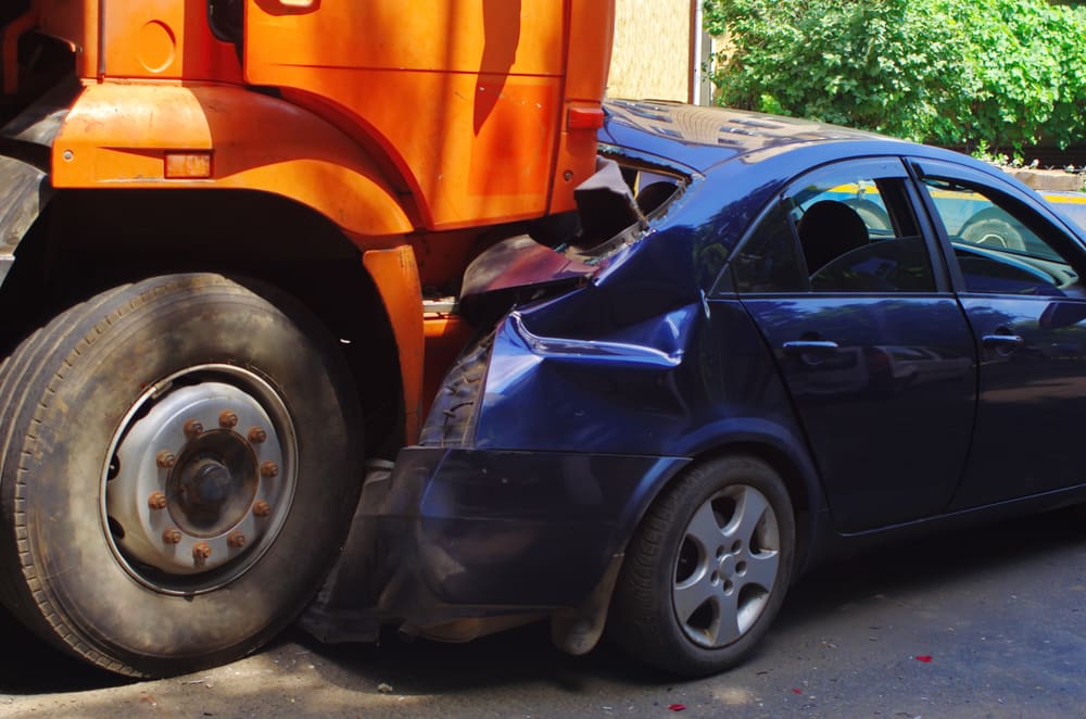 close up of orange semi-truck rear ending a blue sedan