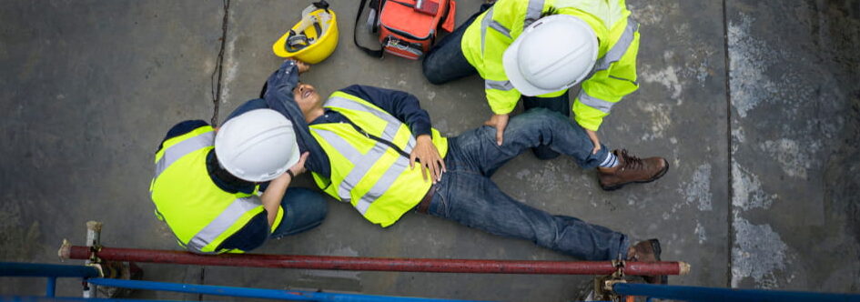 bird's eye view of two construction workers tending to the injuries of a fallen coworkers on the pavement next to a scaffold