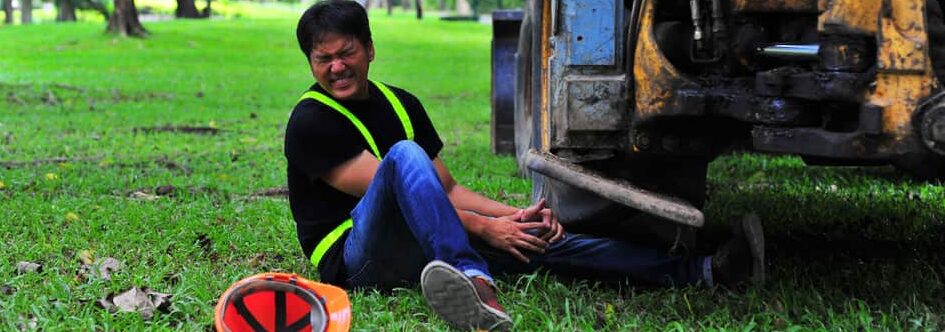 construction worker sitting down in field holding his leg injured by construction vehicle